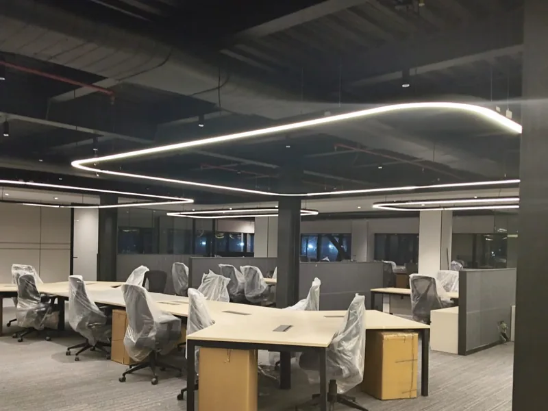 Suspended linear LED ring luminaires over open-plan workstations under an exposed-services ceiling