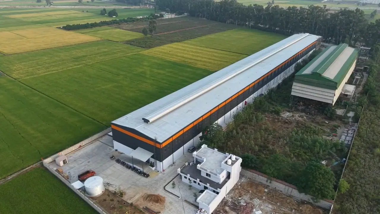 Aerial view of the single-span SBJ Nirmal warehouse, its office block and a water storage tank among fields in Ludhiana district